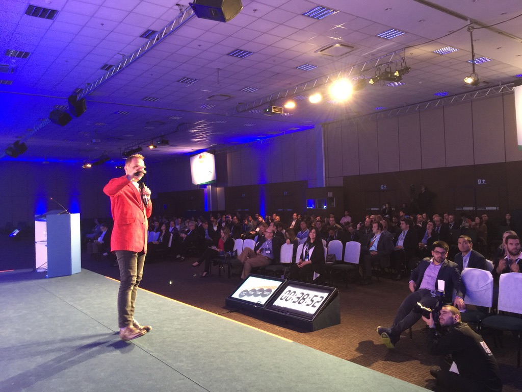 Thoryn Stephens speaking with a handheld microphone in front of a full conference audience